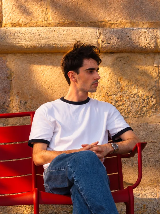 Philippe de Roquefeuil, l'artiste derrière L'atelier Cochevis, assis sur une chaise rouge devant un mur de pierre